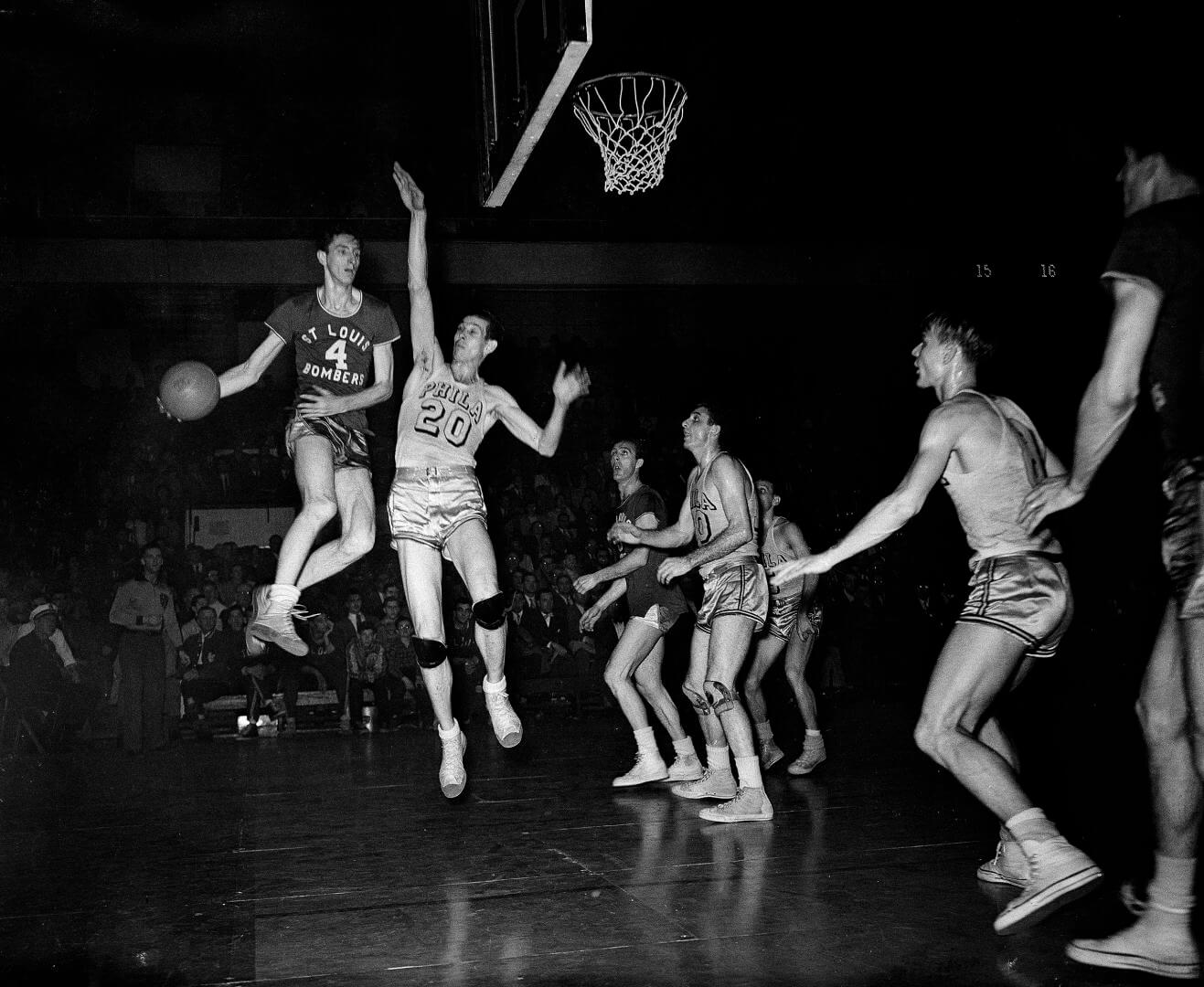Red Rocha (4), St. Louis Bombers center, goes up in the air to make a pass in Basketball Association of America playoff game with the Philadelphia Warriors at the Arena, March 30, 1948. Chuck Halbert, lanky Warriors center, also leaves the floor in an attempt to block the pass. Others are unidentified. (AP Photo/Warren M. Winterbottom)