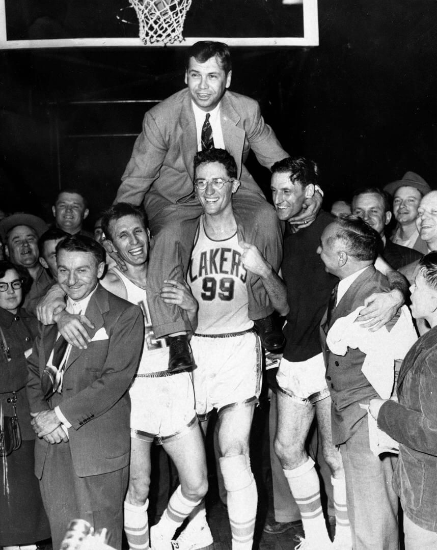 Minneapolis Lakers hoist coach John Kundla and carry him to their dressing room after beating the New York Knickebockers 82-65 April 25, 1952, and winning their fourth National Basketball Association title in five years.Left to right are Max Winter, Laker manager (dark suit); Slater Martin (22); George Mikan (99) ; Jim Pollard ( sweatshirt) and Ben Berger Laker president. (AP Photo)