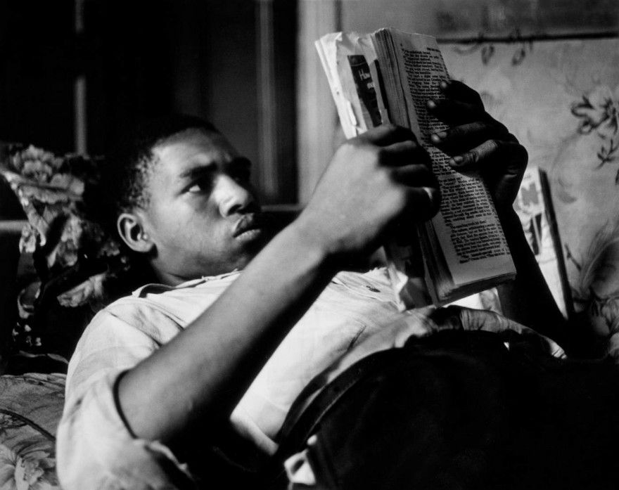 Chico negro leyendo en la cama capturado por Gordon parks