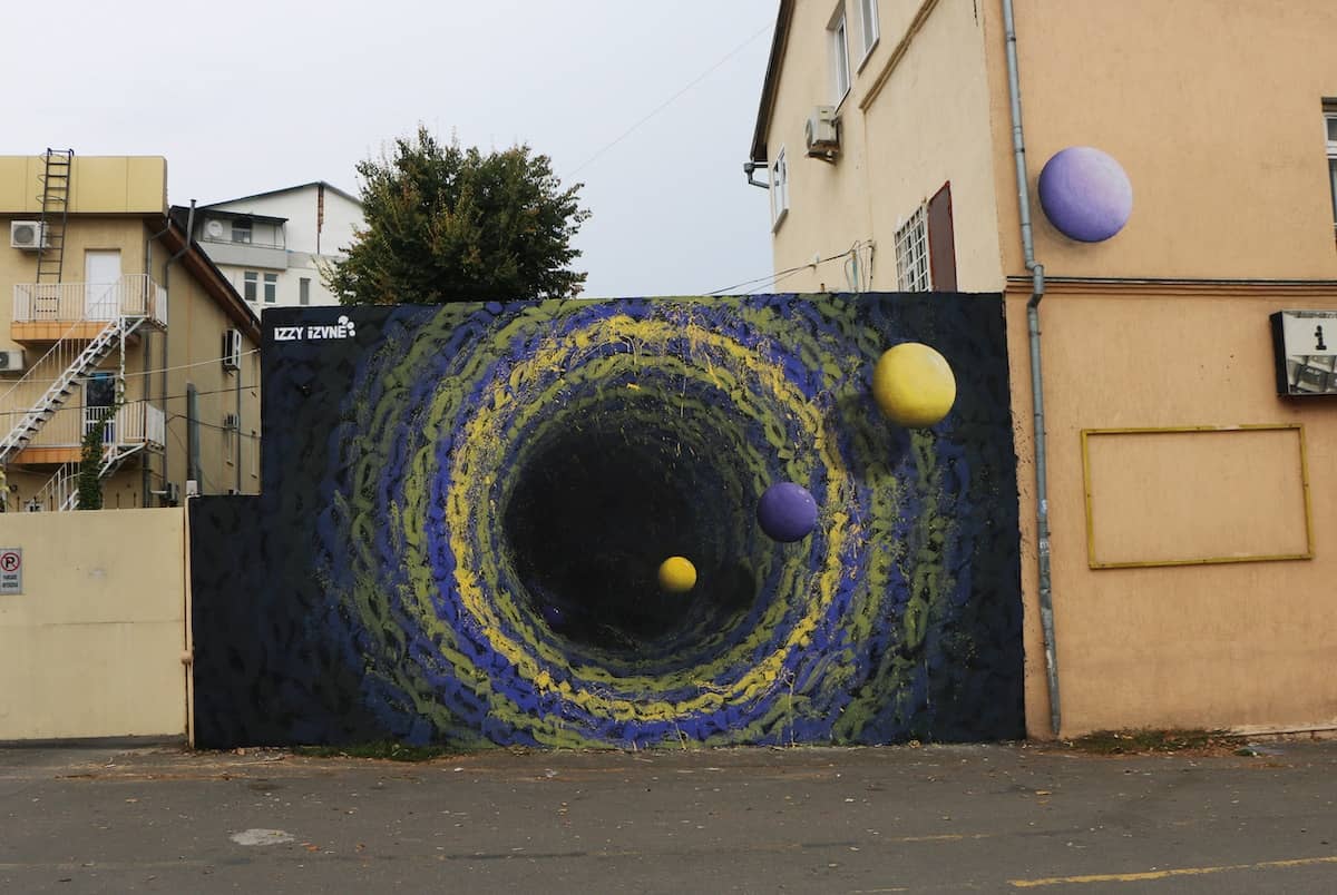 mural colorido de un agujero negro street art de Izzi Izvne
