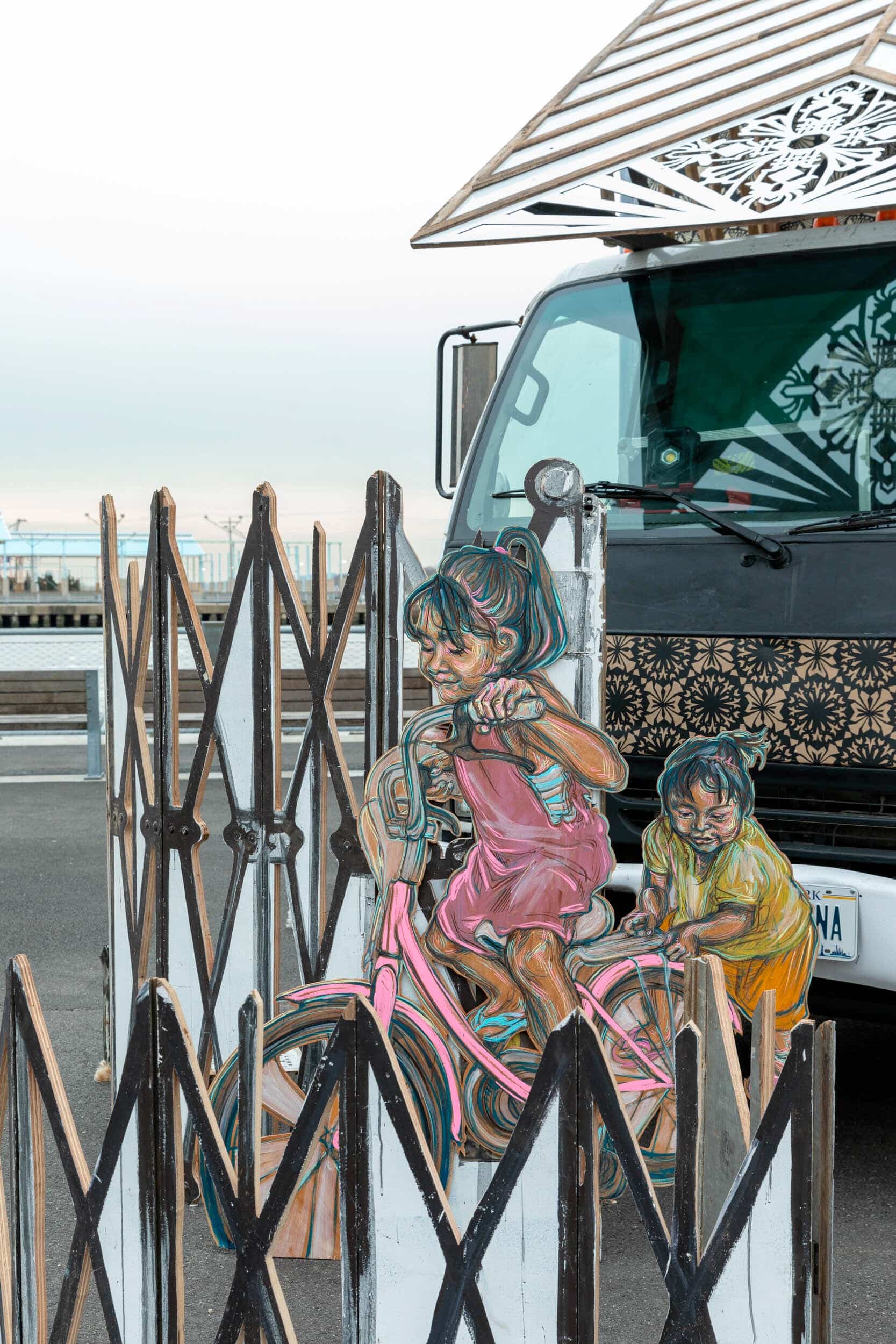 niña montando en bicicleta y niña empujando, figuras bidimensioanles de la obra de swoon